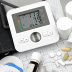 Digital blood pressure monitor on ECG paper with pills and medical supplies, ideal for healthcare topics.