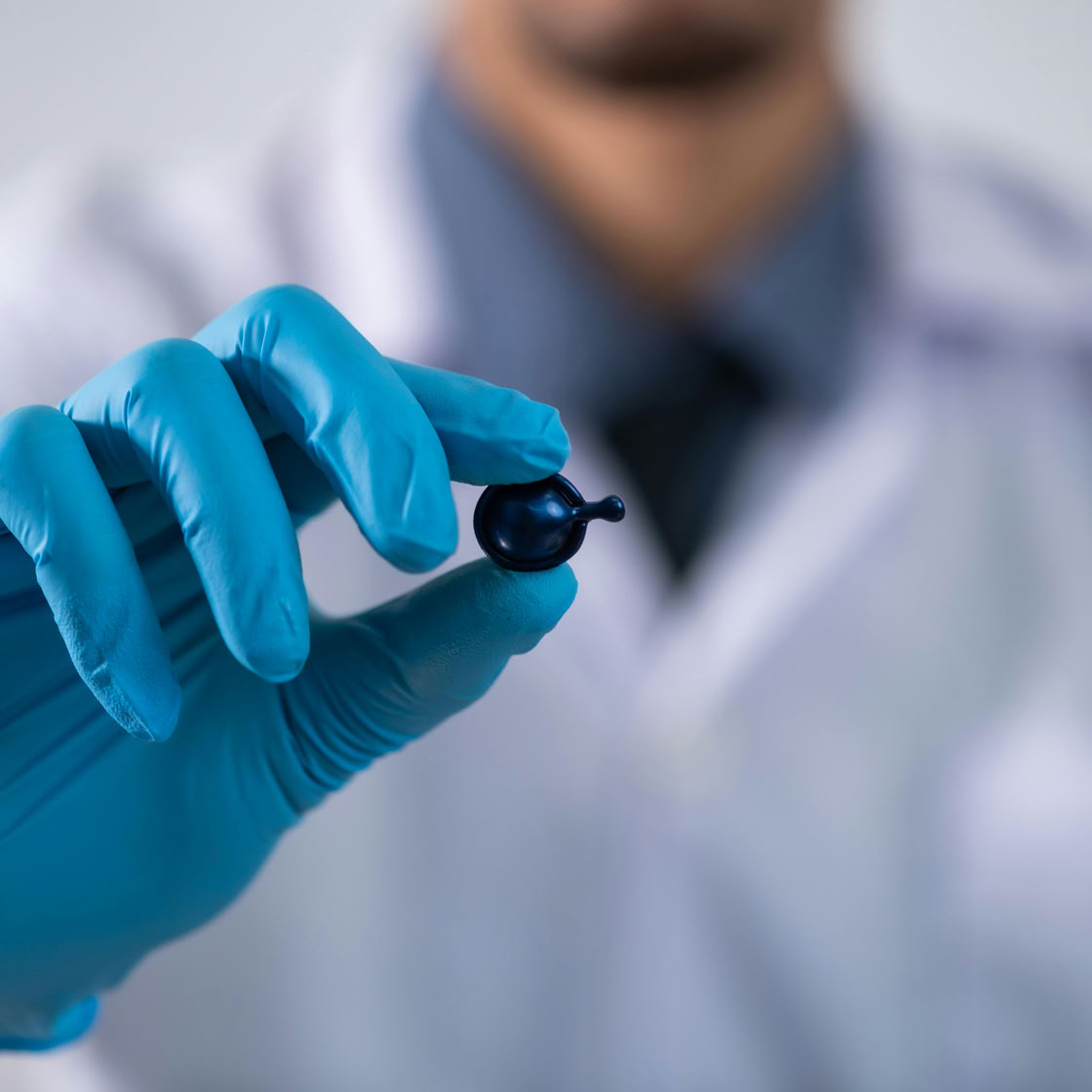 A scientist wearing gloves holding a small capsule in a laboratory setting, showcasing healthcare and research.