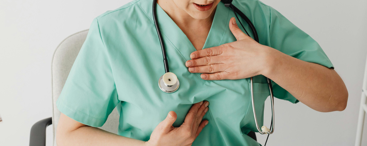 A female doctor in scrubs wearing headphones conducts an online consultation.