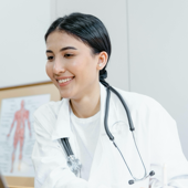 Confident female doctor in a lab coat smiling during an online consultation using a laptop.